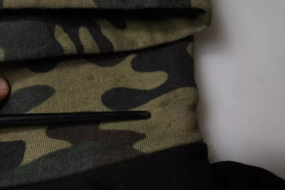 Un objet cylindrique noir lisse posé sur un tissu camouflage plié avec un sweat à capuche camouflage noir dolce & gabbana