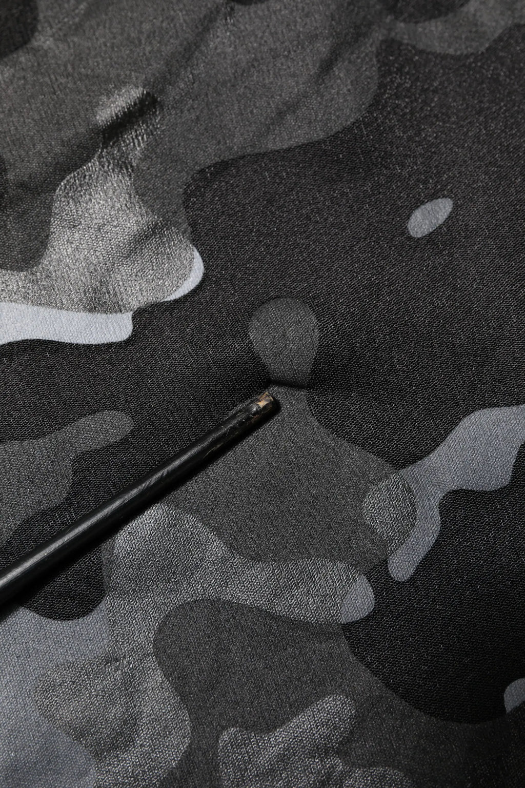 Crayon noir avec embout métallique posé sur tissu camouflage gris foncé du pull dolce & gabbana noir