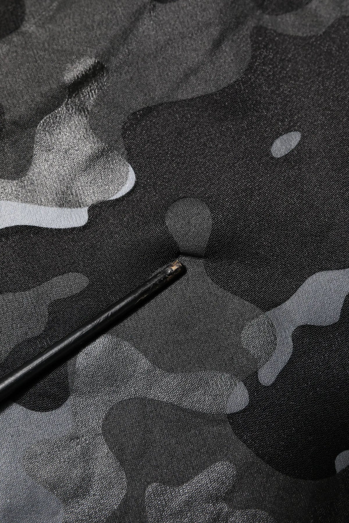 Crayon noir avec embout métallique posé sur tissu camouflage gris foncé du pull dolce & gabbana noir