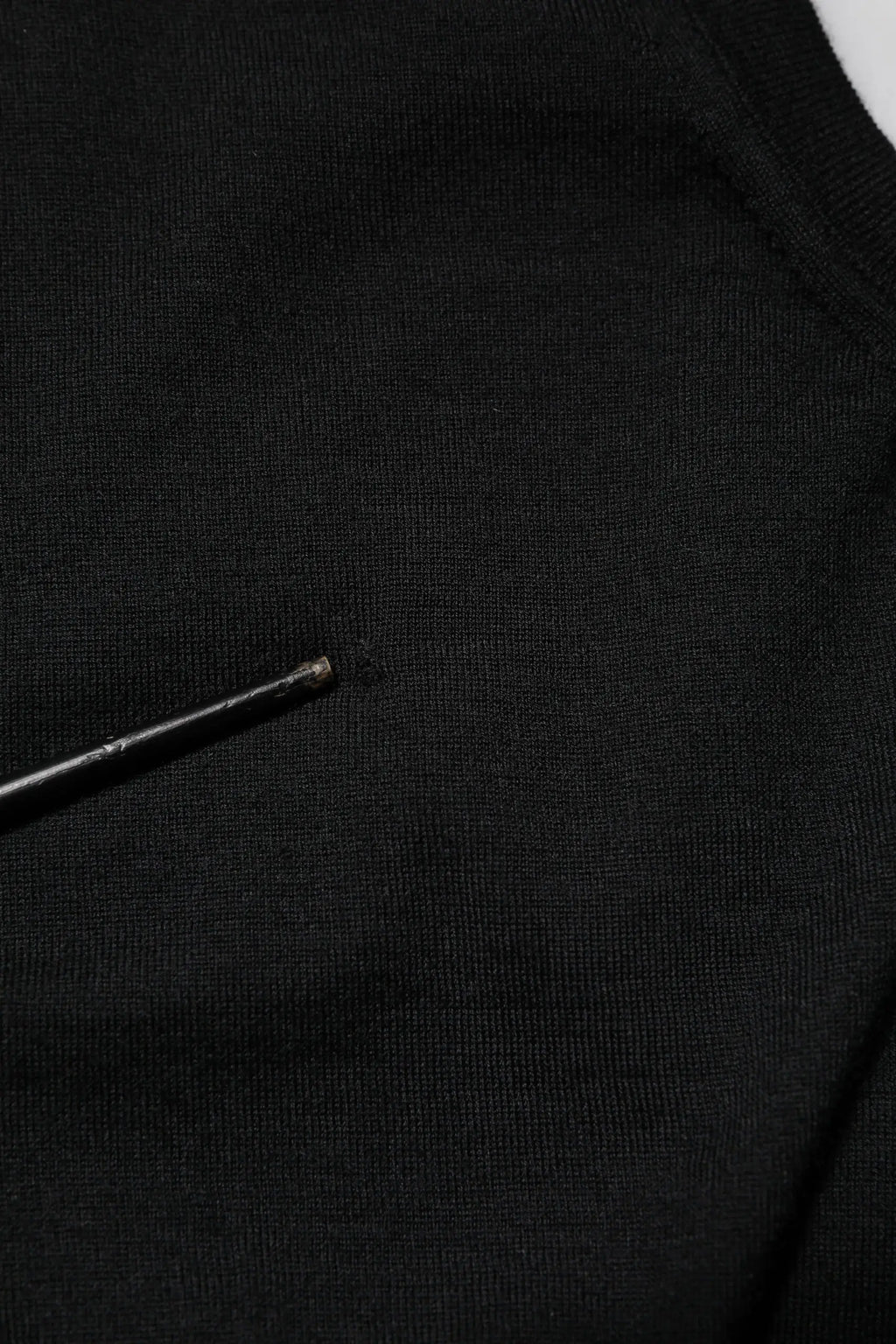 Tissu noir en maille avec une petite aiguille métallique reposant sur un débardeur sans manches en cachemire noir dolce & gabbana