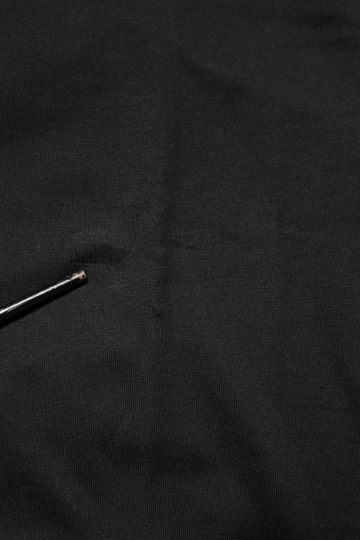Une aiguille métallique élégante avec une pointe argentée polie reposant sur un débardeur homme en coton noir dolce gabbana