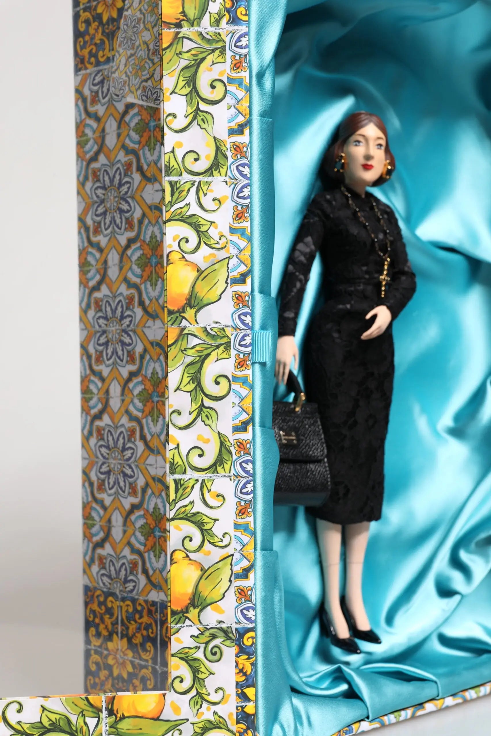 Robe noire en dentelle à silhouette ajustée et manches longues portée par poupée dans boîte ornée doublée de satin turquoise dolce gabbana