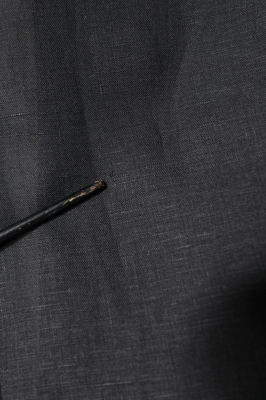 Crayon noir avec pointe usée posé sur tissu gris foncé texturé près d’un manteau blazer homme dolce gabbana noir en lin simple boutonnage