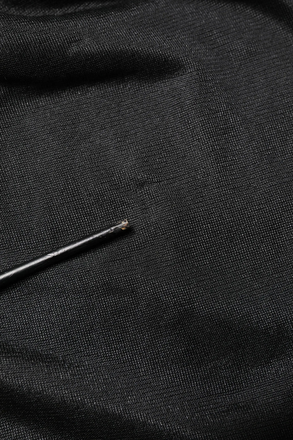 Aiguille noire reposant sur tissu texturé foncé du pull à col rond en maille avec logo noir dolce & gabbana