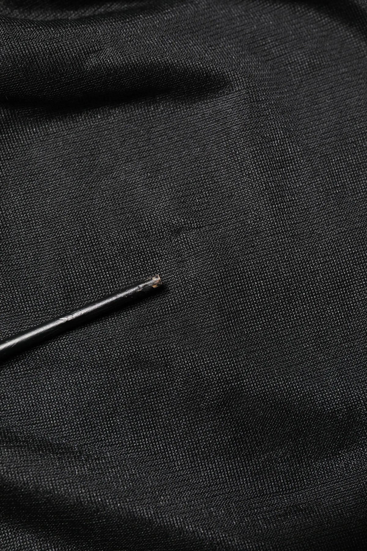 Aiguille noire reposant sur tissu texturé foncé du pull à col rond en maille avec logo noir dolce & gabbana