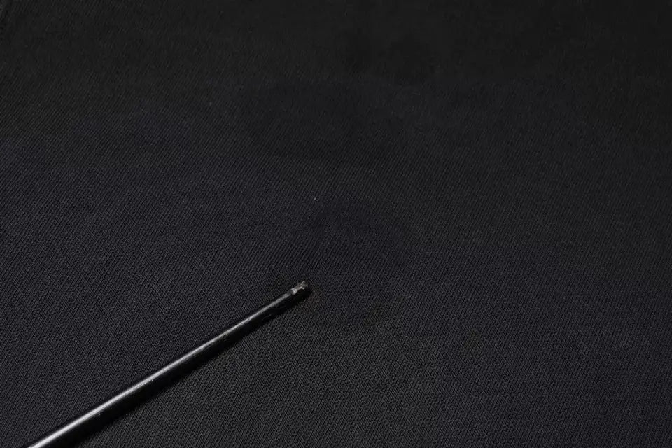 Bâtonnet noir mince avec embout arrondi posé sur tissu foncé près d’un sweat à capuche zippé dolce & gabbana noir avec logo plaque