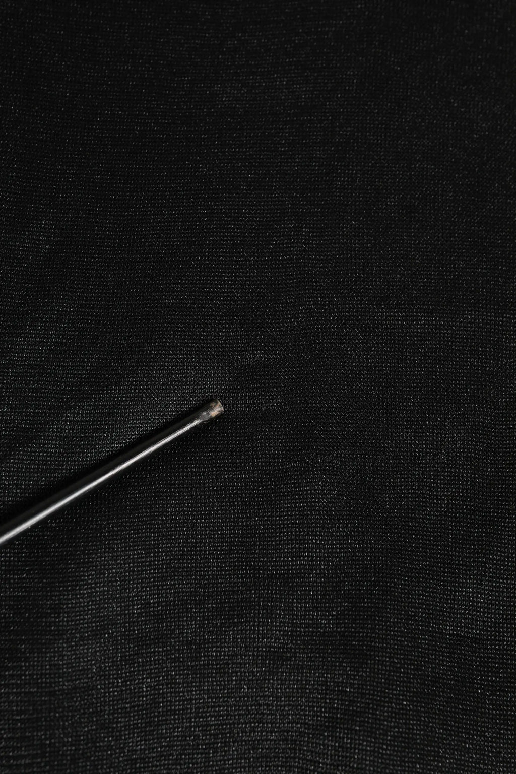 Une aiguille métallique fine avec une pointe tranchante posée sur un sweat noir en polyester dolce & gabbana avec logo