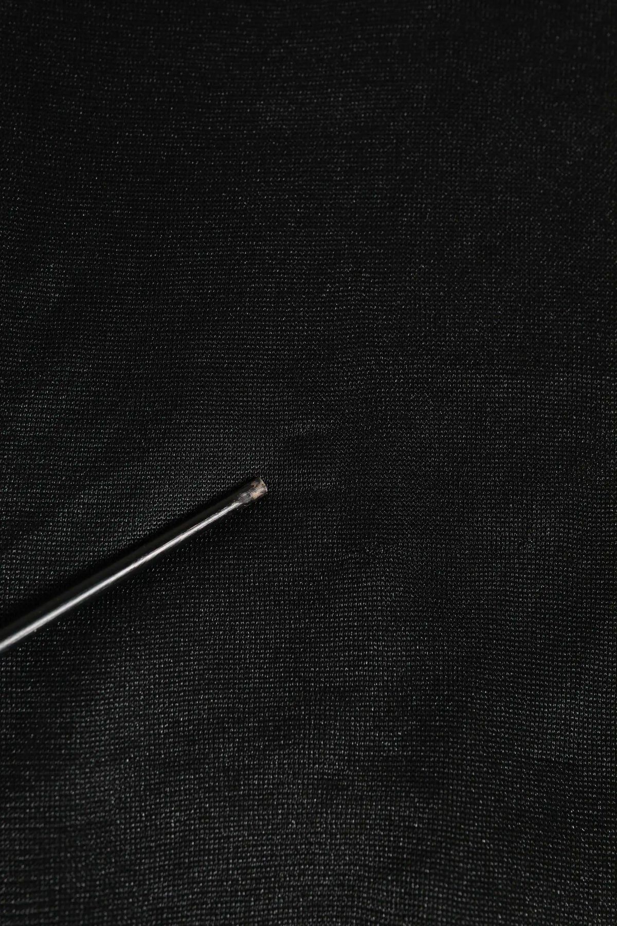 Une aiguille métallique fine avec une pointe tranchante posée sur un sweat noir en polyester dolce & gabbana avec logo