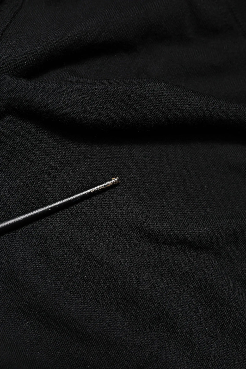 Une aiguille métallique fine à finition argentée posée en diagonale sur un pull dolce & gabbana noir à manches longues col rond en tissu doux