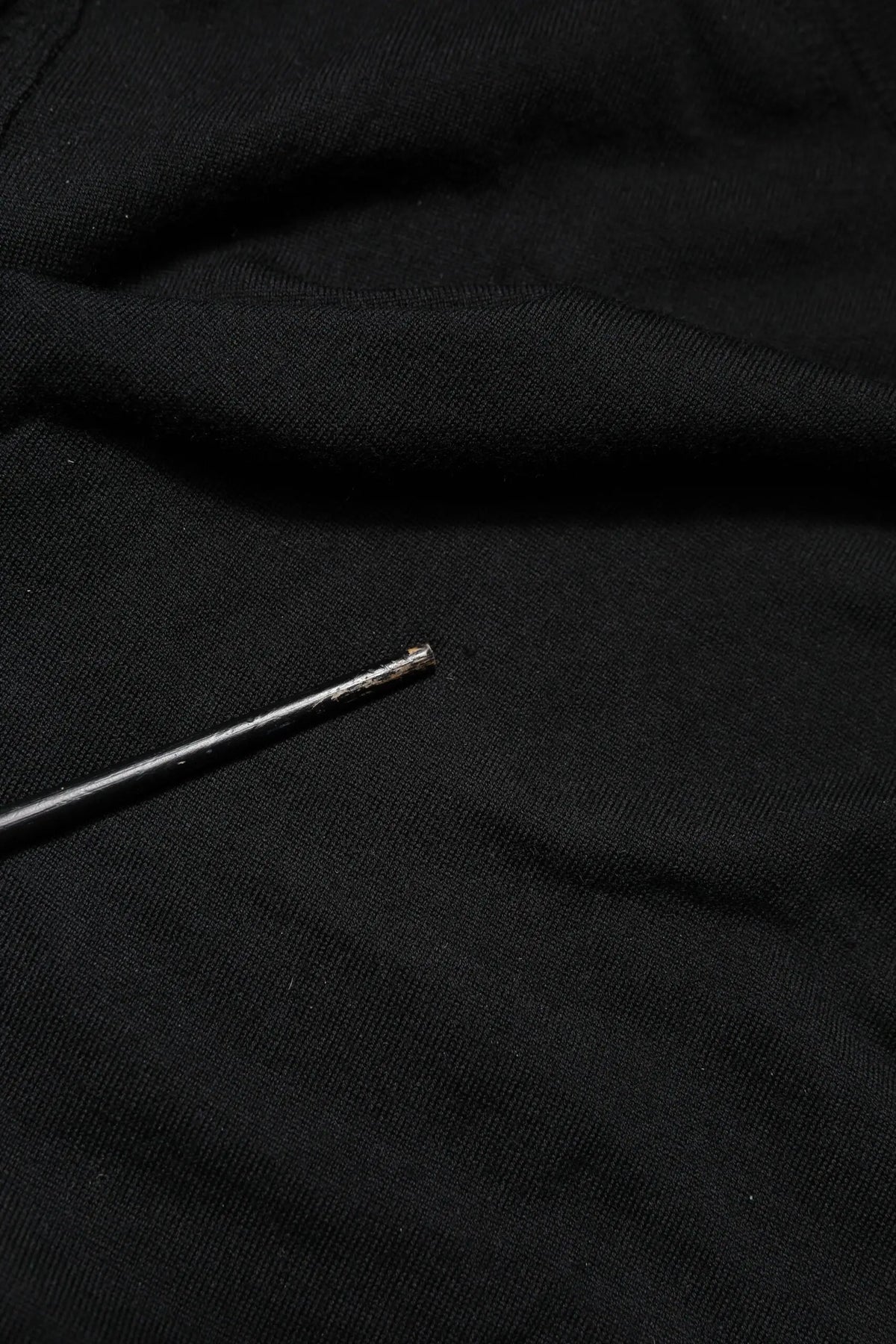 Une aiguille métallique fine à finition argentée posée en diagonale sur un pull dolce & gabbana noir à manches longues col rond en tissu doux