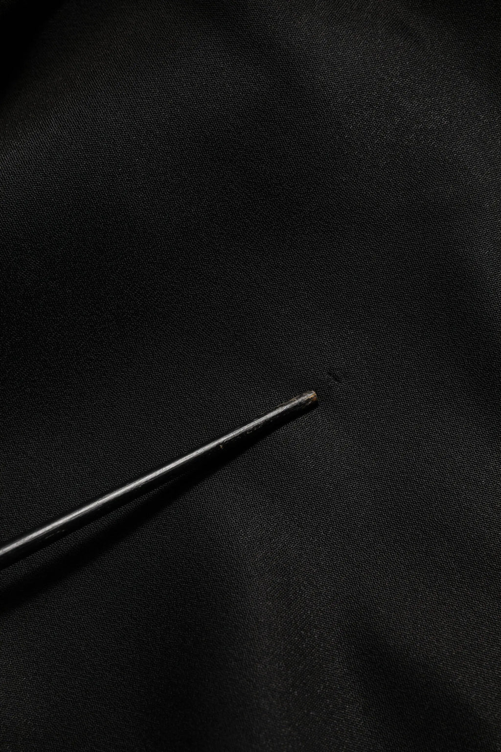 Une aiguille noire fine posée sur un tissu foncé avec un pull dolce & gabbana noir logo dg en cristal