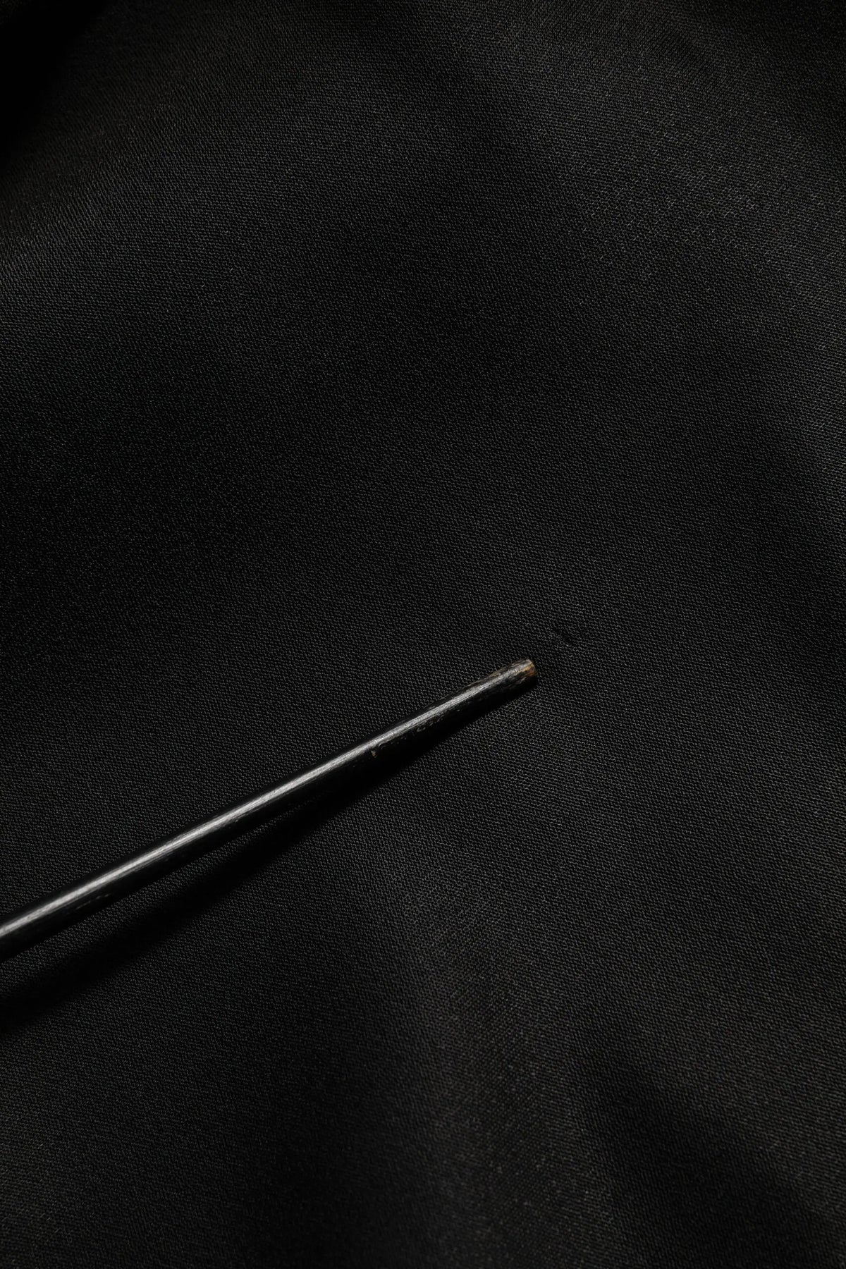 Une aiguille noire fine posée sur un tissu foncé avec un pull dolce & gabbana noir logo dg en cristal