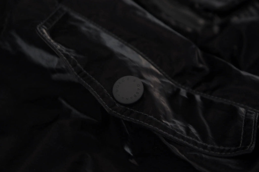 Un bouton noir mat avec des gravures subtiles sur une poche en tissu noir brillant du bomber dolce & gabbana en nylon