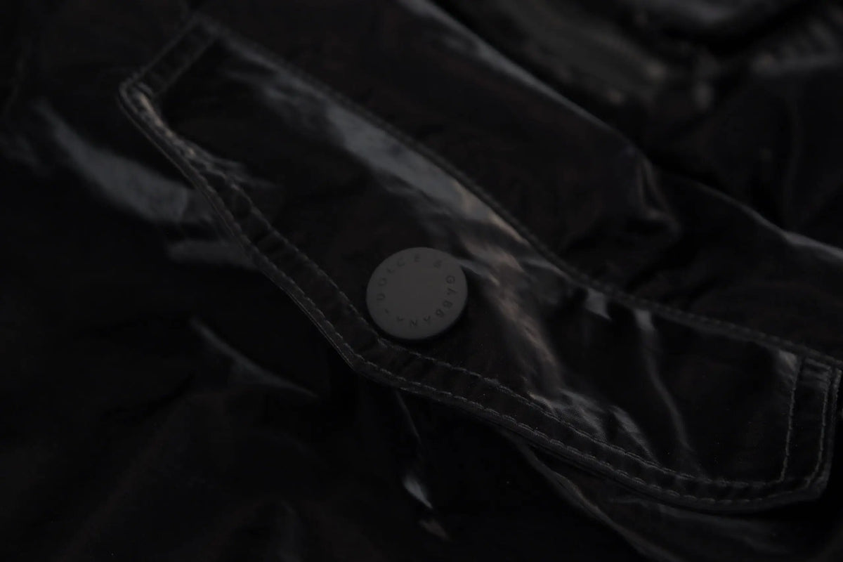 Un bouton noir mat avec des gravures subtiles sur une poche en tissu noir brillant du bomber dolce & gabbana en nylon