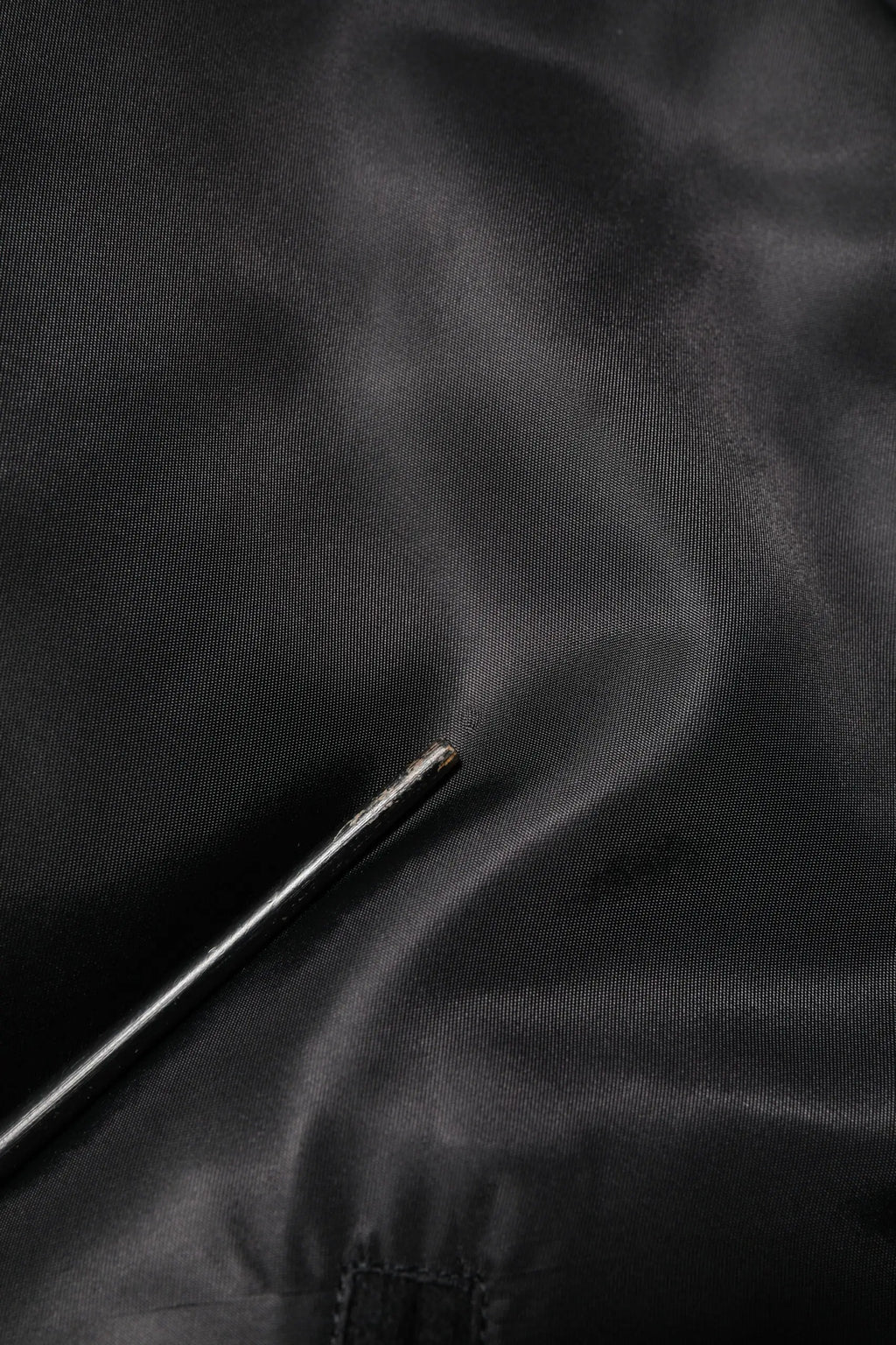 Une aiguille métallique argentée repose sur un tissu satin noir sous un bomber dolce & gabbana noir en polyester avec logo plaque