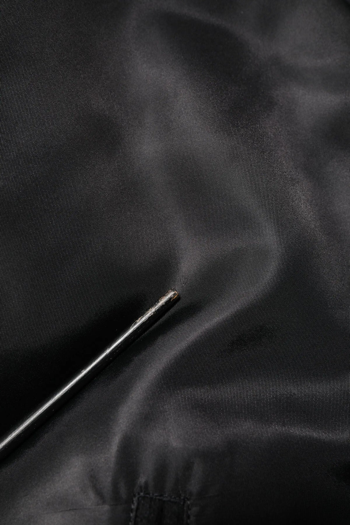 Une aiguille métallique argentée repose sur un tissu satin noir sous un bomber dolce & gabbana noir en polyester avec logo plaque