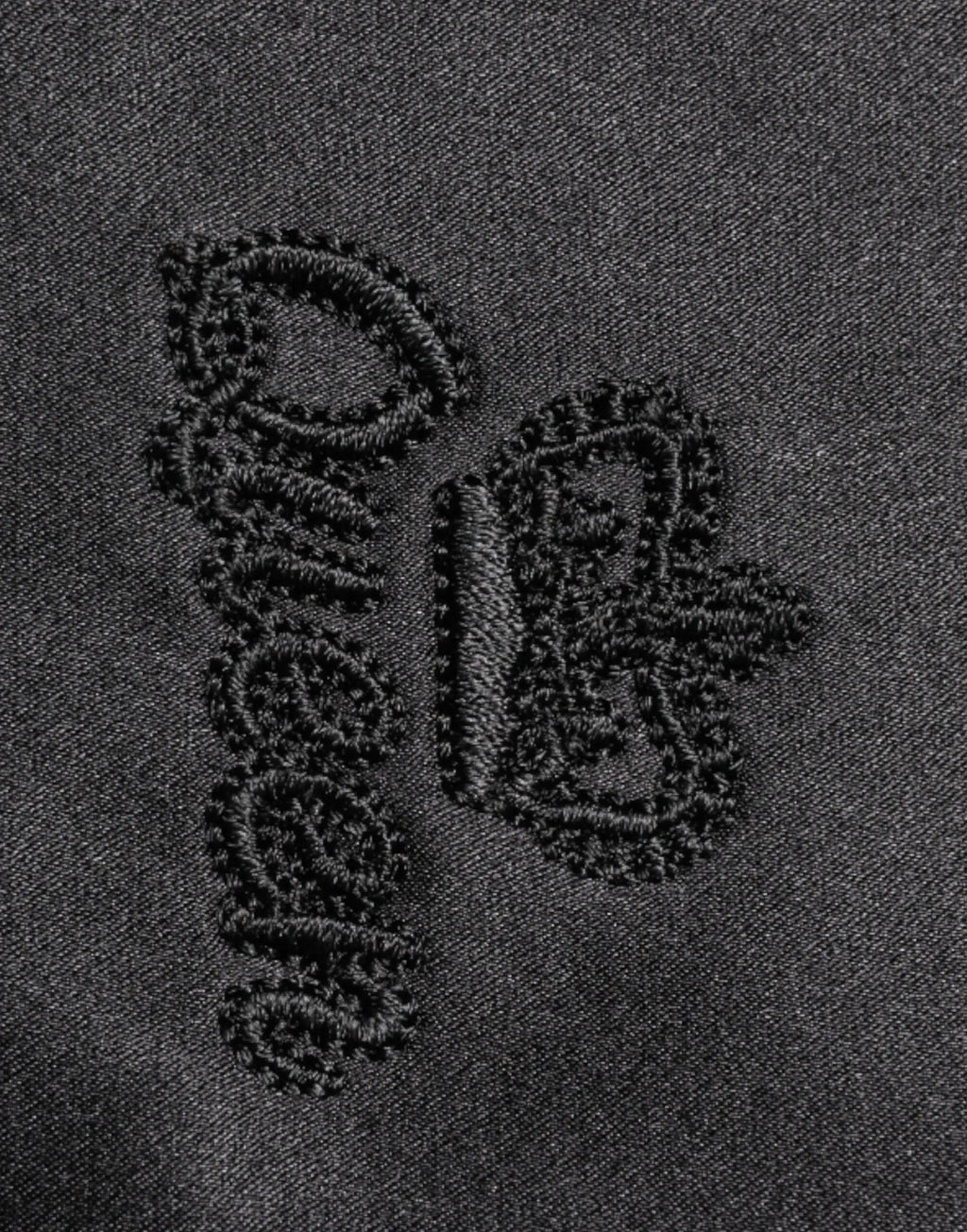 Logo brodé noir sur tissu denim foncé du chemisier dolce & gabbana en soie noire avec col ascot et boutons