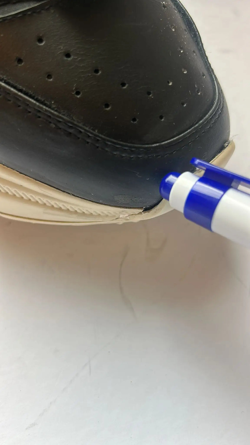 Un marqueur bleu et blanc est utilisé pour marquer le bord d’une chaussure basse en cuir noir dolce & gabbana daymaster