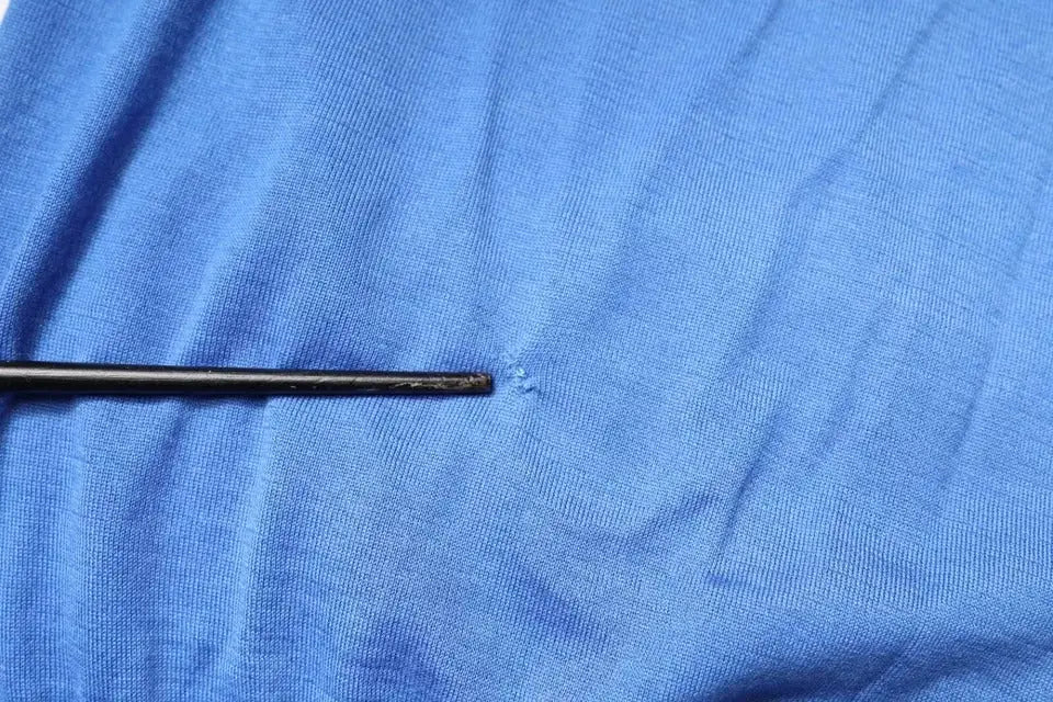 Une aiguille noire fine posée horizontalement sur un tissu bleu texturé du polo dolce & gabbana manches courtes col bleu