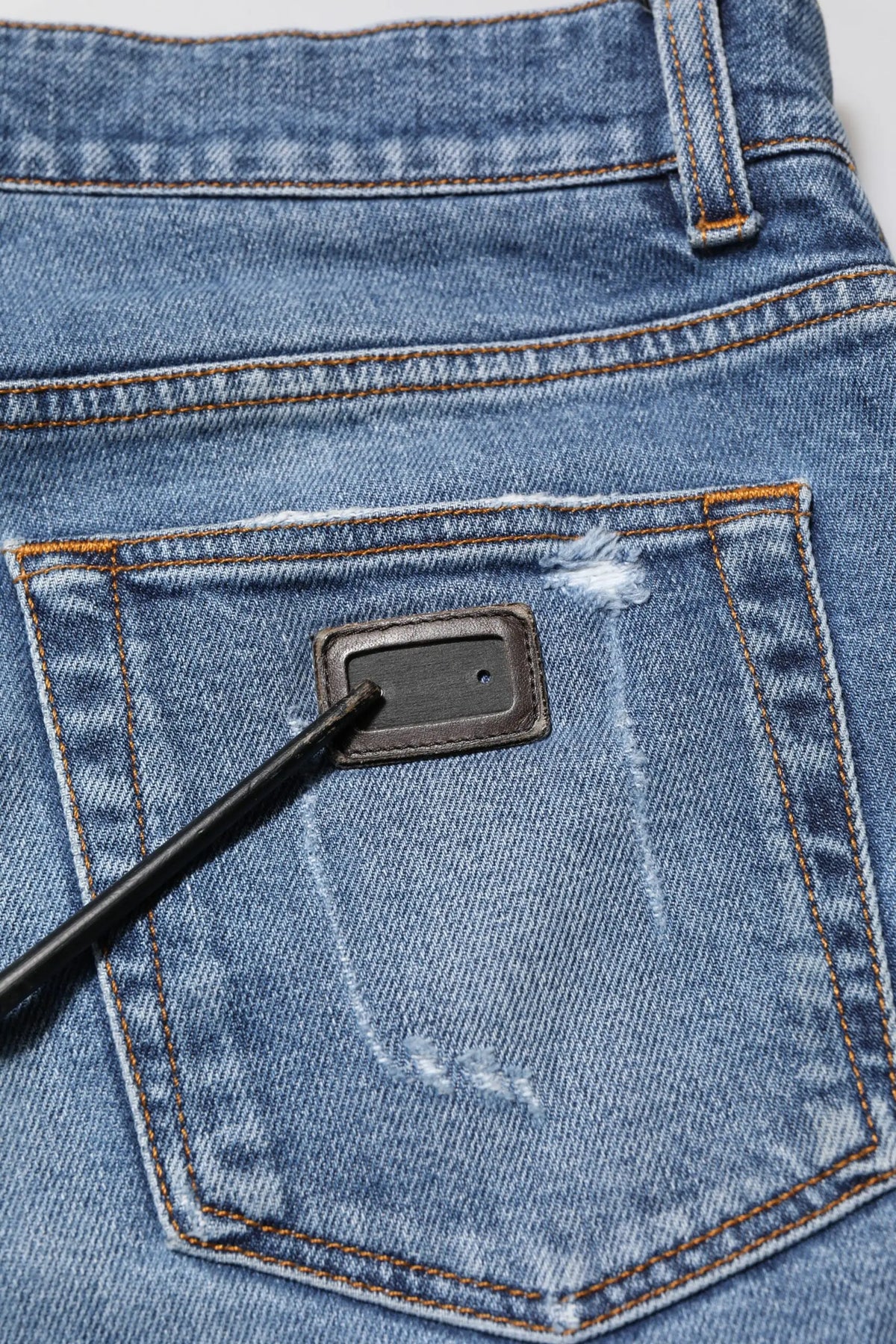 Jeans en denim bleu dolce & gabbana en coton avec poche arrière déchirée, patch en cuir noir et couture orange
