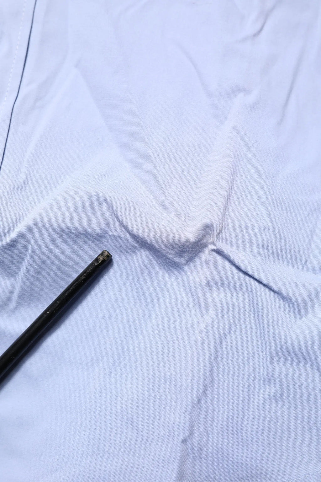 Objet cylindrique noir avec extrémité usée posé sur tissu blanc à côté d’une chemise longue bleue en coton dolce & gabbana sicilia