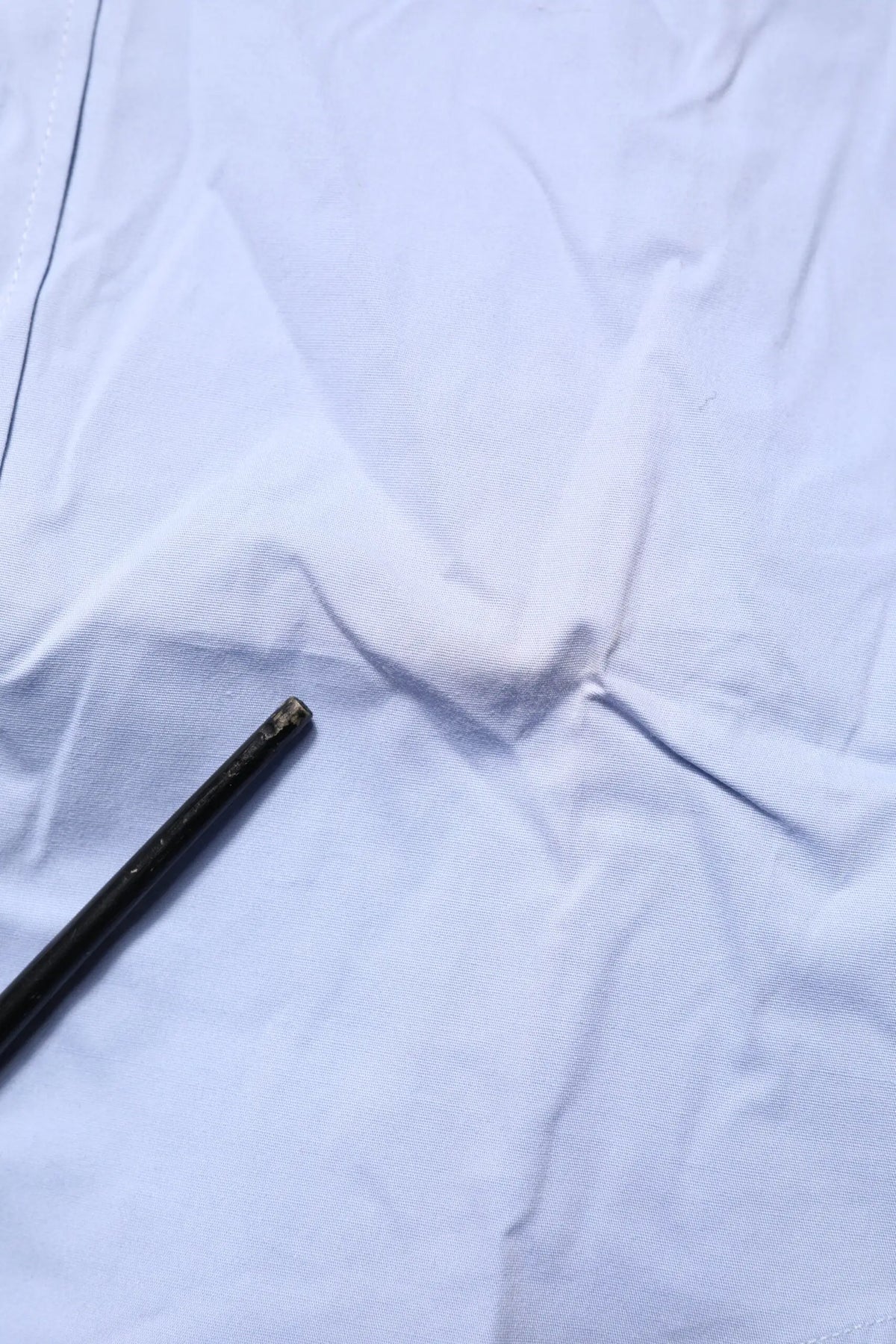Objet cylindrique noir avec extrémité usée posé sur tissu blanc à côté d’une chemise longue bleue en coton dolce & gabbana sicilia