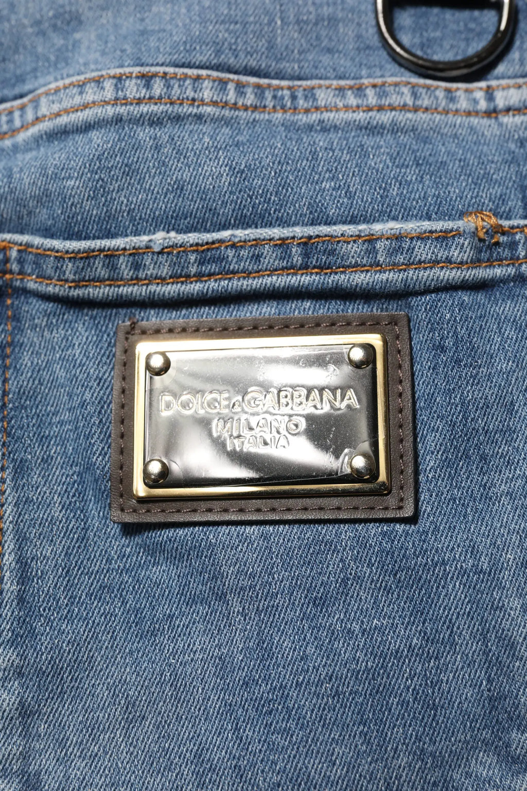 Plaque rectangulaire métallique dolce & gabbana milano italia encadrée de cuir marron foncé sur jean denim skinny bleu en coton déchiré