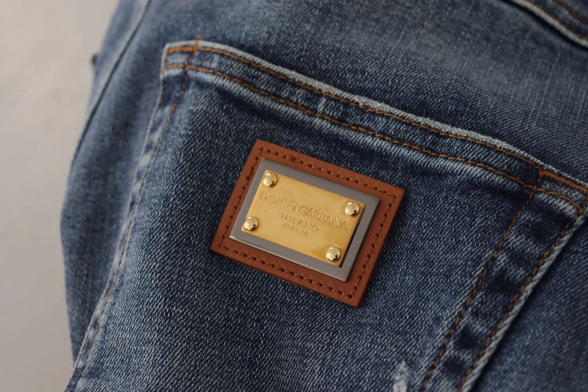Un patch rectangulaire en cuir marron avec une plaque métal dorée dolce gabbana milano cousue sur un jean en denim bleu foncé crystalisé