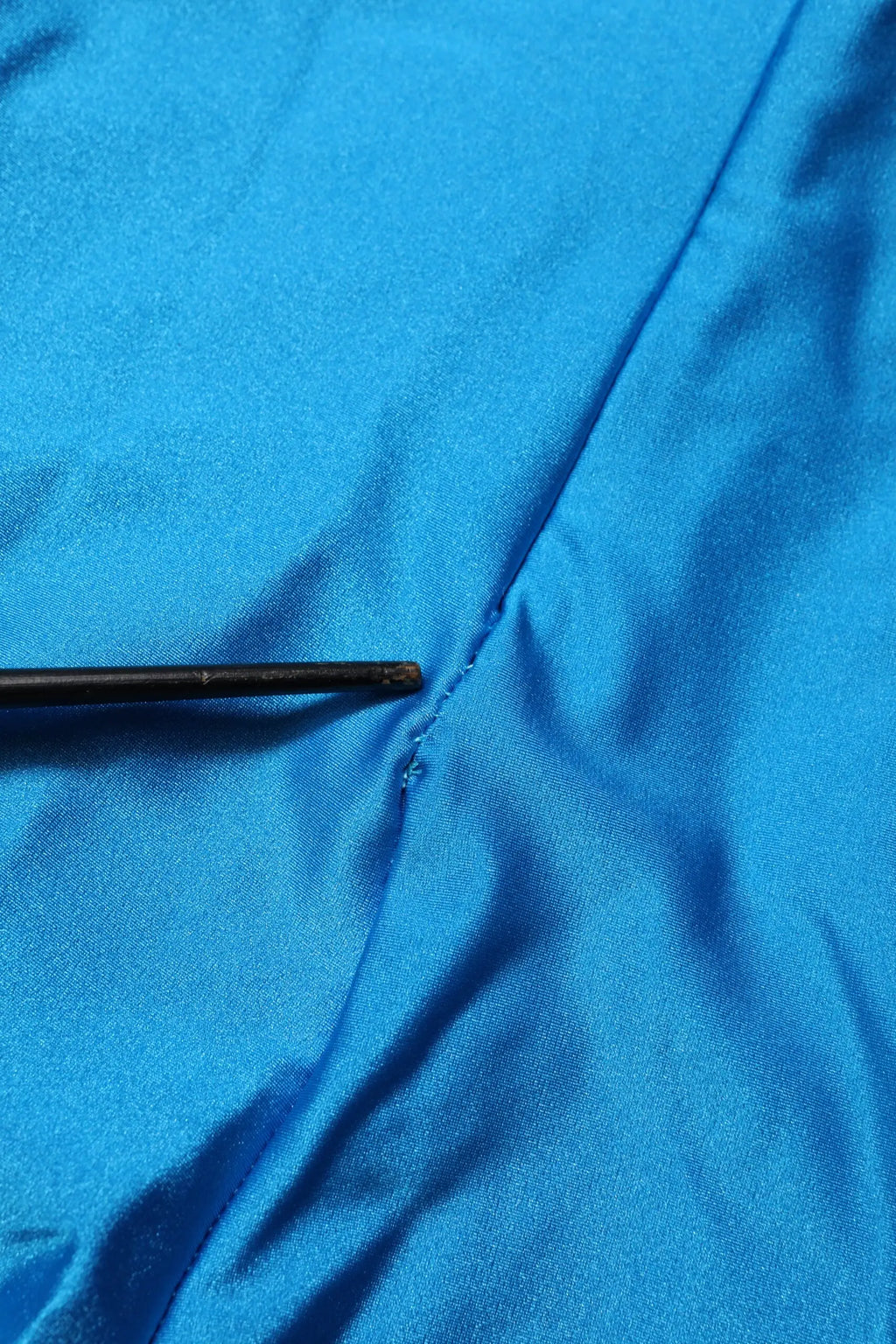 Une aiguille noire posée sur un tissu satin bleu éclatant à côté d’une combinaison robe moulante col roulé en nylon bleu dolce & gabbana