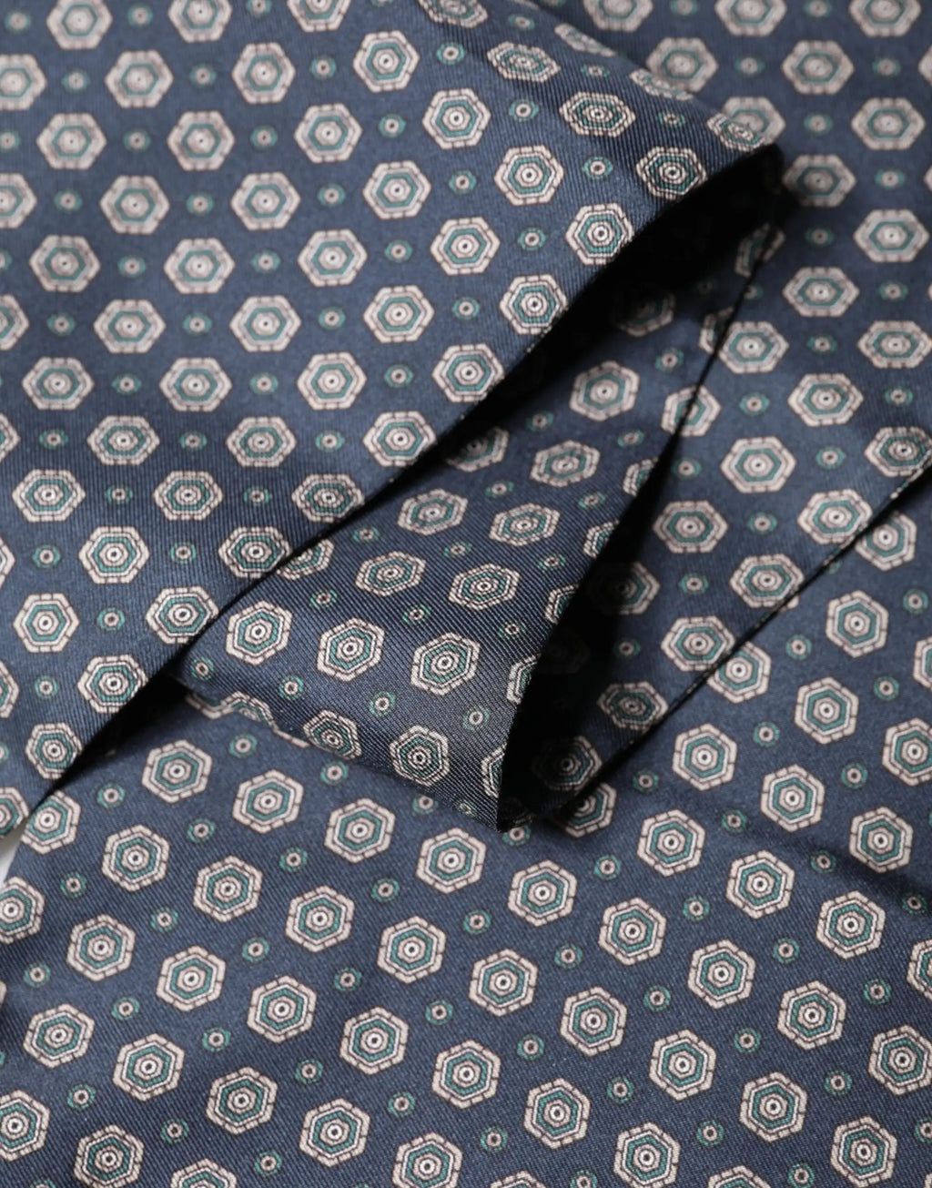 Une cravate en soie bleu marine avec un motif hexagonal géométrique répétitif en teal et blanc