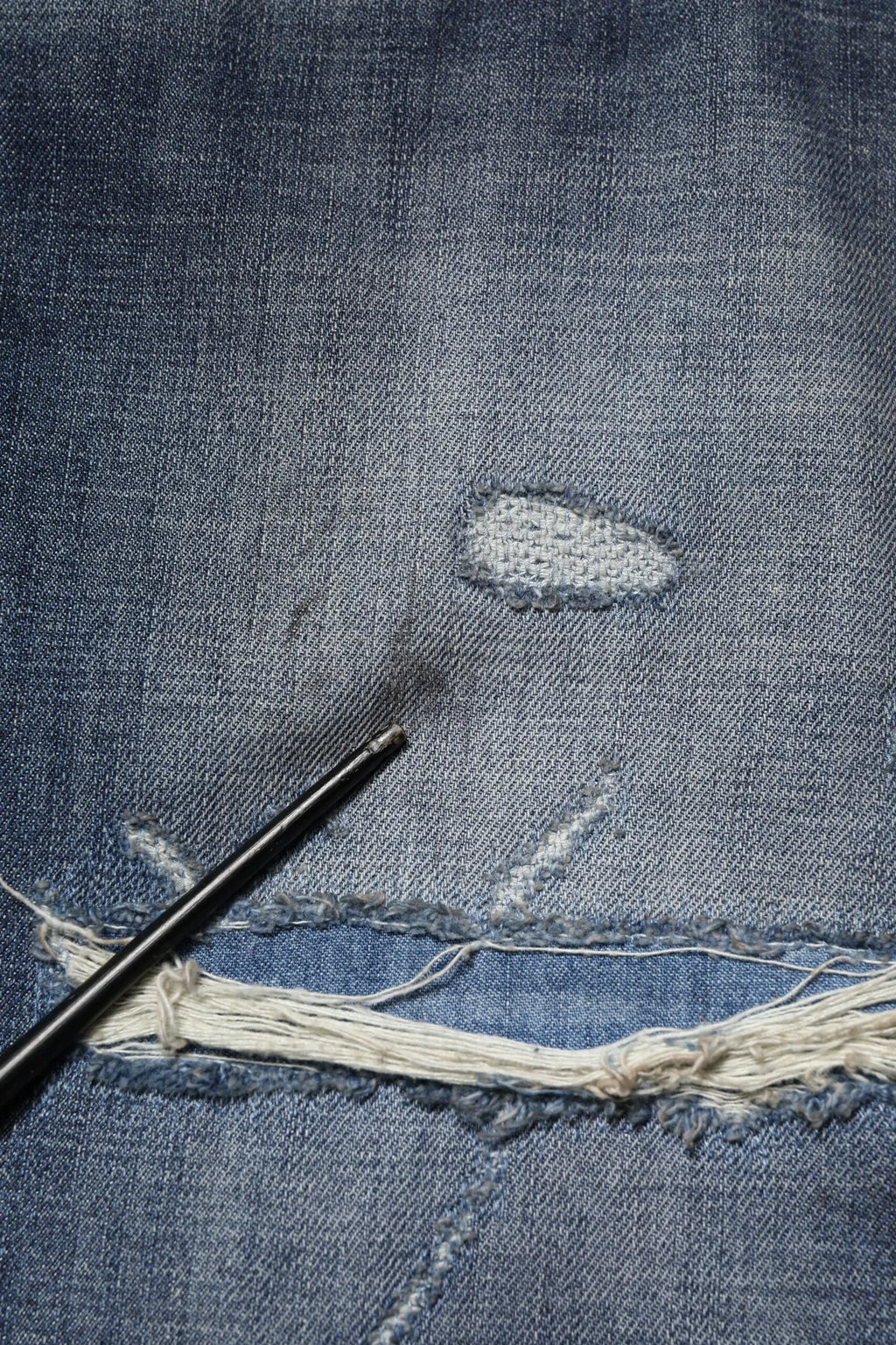 Un crochet noir repose sur un jean homme dolce gabana en coton bleu délavé avec bords effilochés et réparation brodée