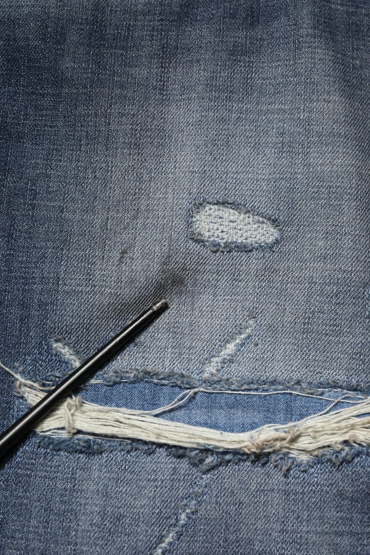 Un crochet noir repose sur un jean homme dolce gabana en coton bleu délavé avec bords effilochés et réparation brodée