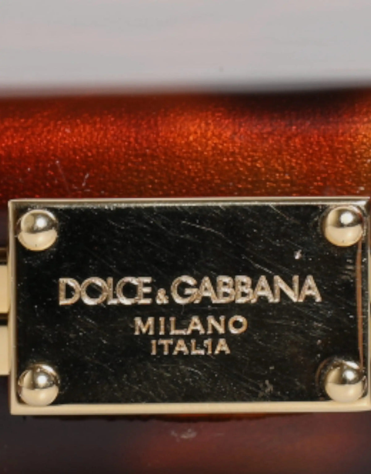 Plaque en cuir noir avec lettres dorées et rivets portant le logo dolce & gabbana milano italia sur pochette marron en cuir