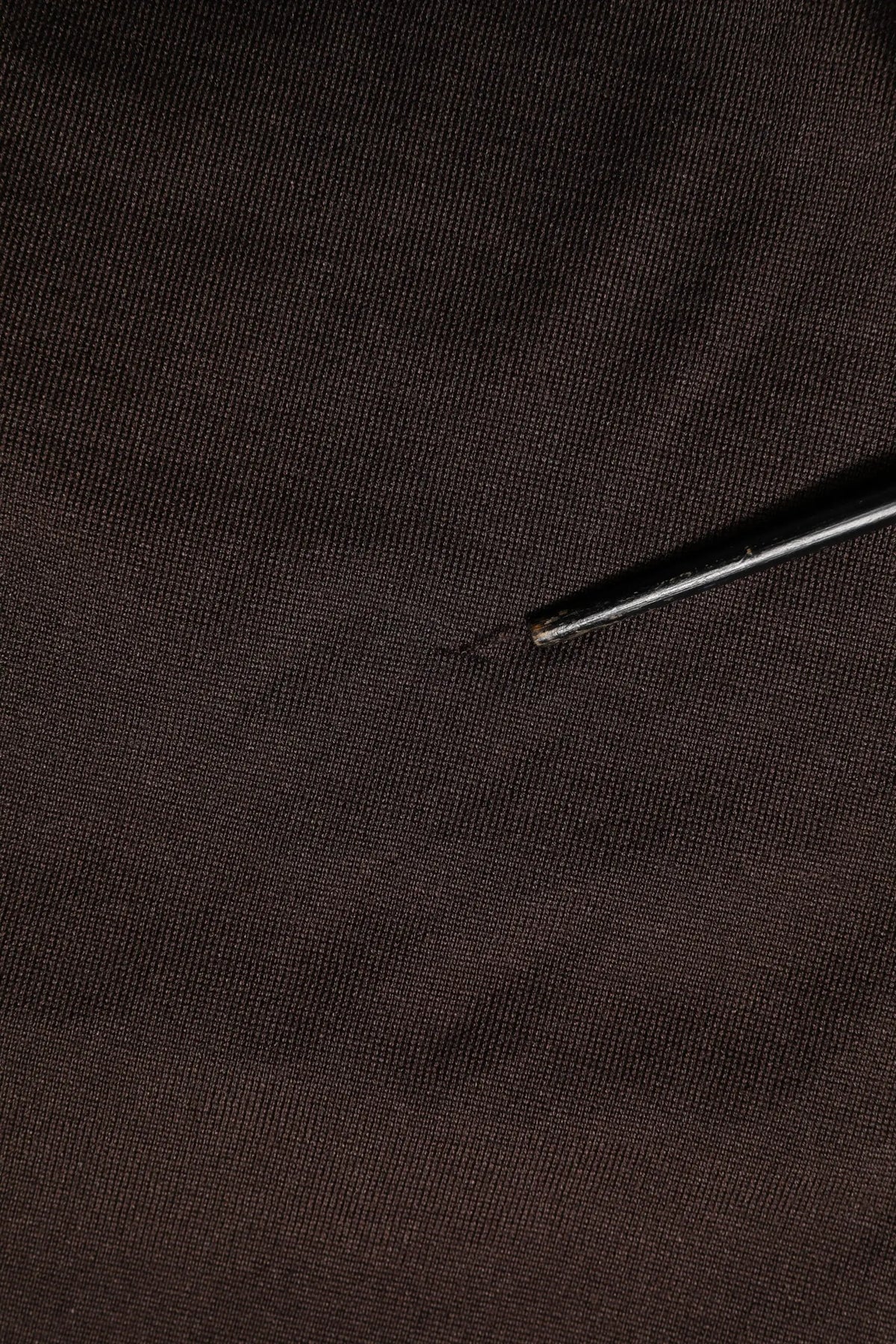 Une aiguille en metal noir repose diagonalement sur un tissu tisse marron fonce pour le t shirt dolce & gabbana en soie marron manches courtes col rond