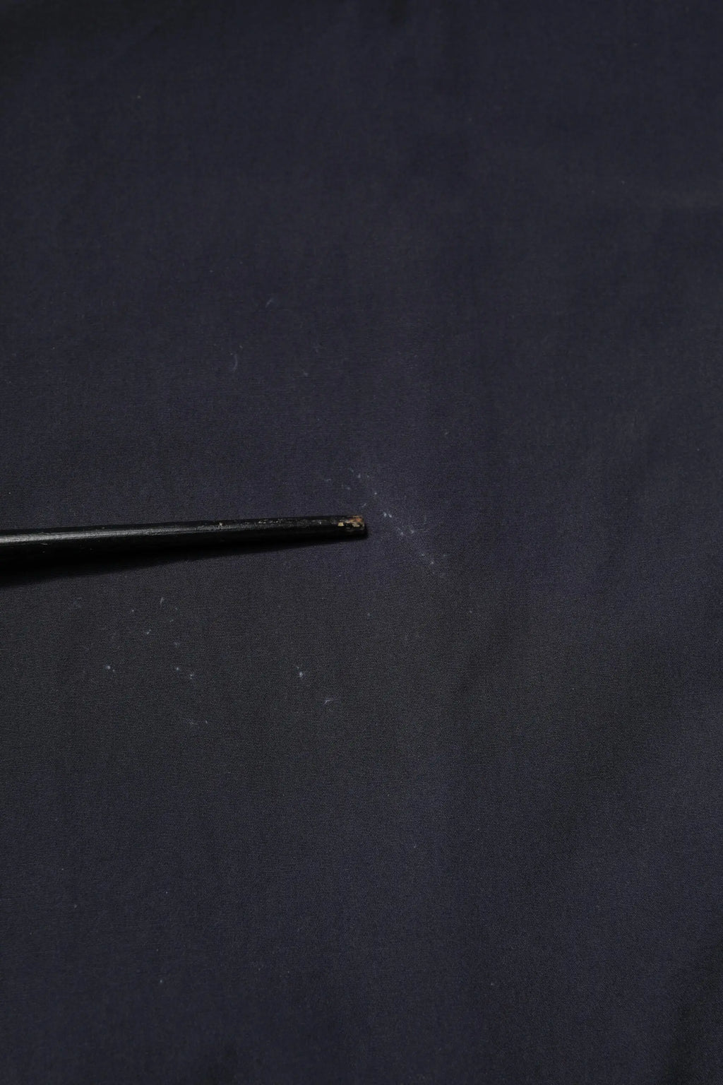 Aiguille noire en métal avec pointe légèrement usée posée sur surface sombre près chemise décontractée bleu foncé en coton dolce gabbana manches courtes