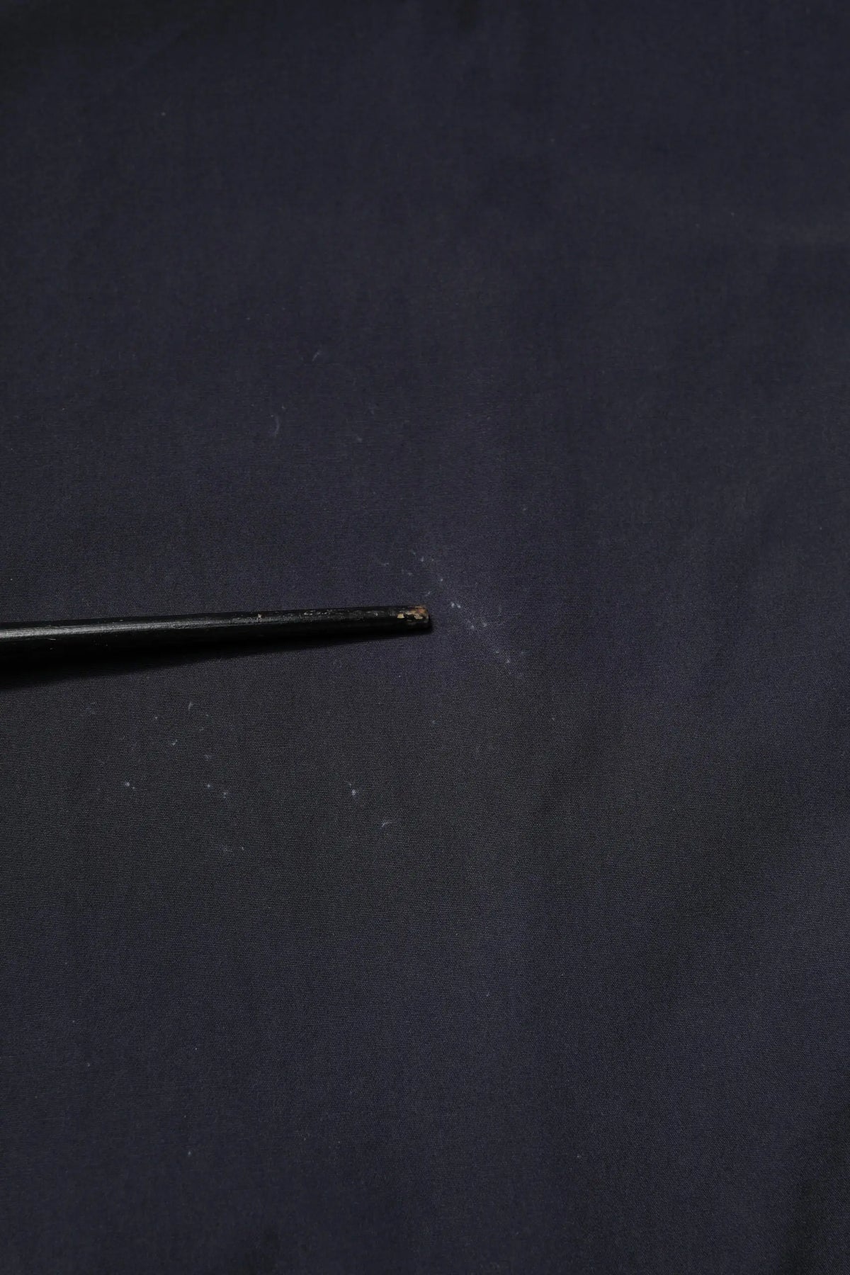 Aiguille noire en métal avec pointe légèrement usée posée sur surface sombre près chemise décontractée bleu foncé en coton dolce gabbana manches courtes