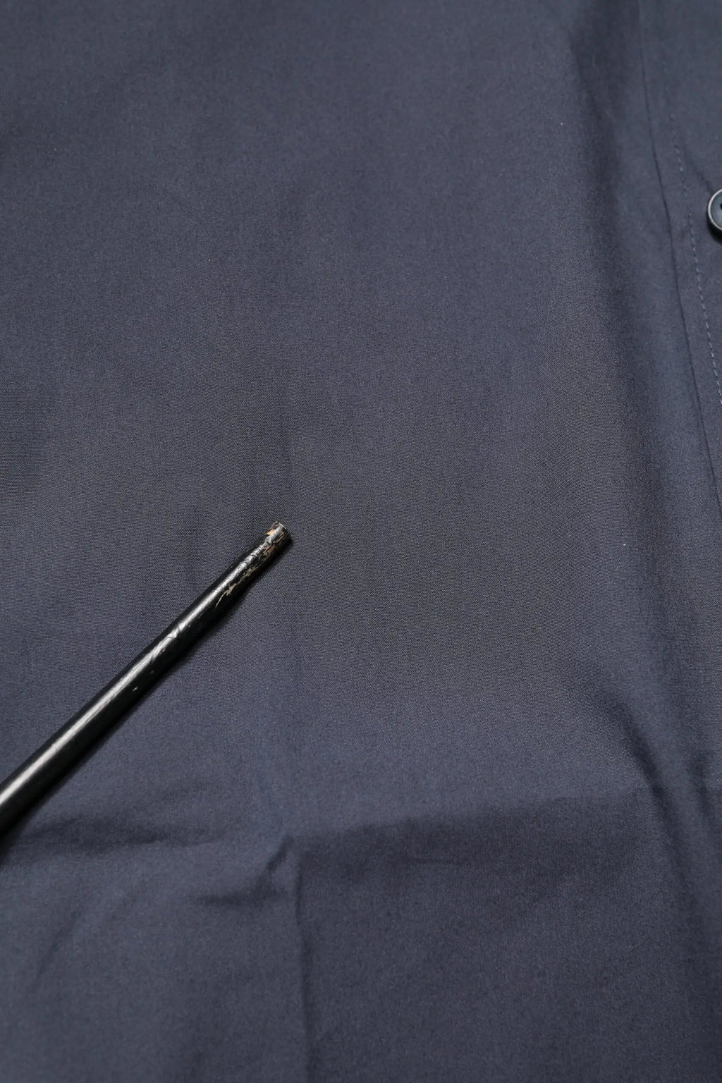 Un outil noir en métal avec une prise texturée et une pointe est posé sur un tissu foncé à côté d’une chemise formelle dolce & gabbana bleu foncé en coton gold