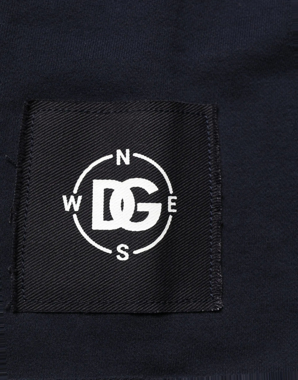 Étiquette noire tissée avec logo dg brodé blanc entouré de points de compas sur sweat en coton bleu foncé dolce & gabbana