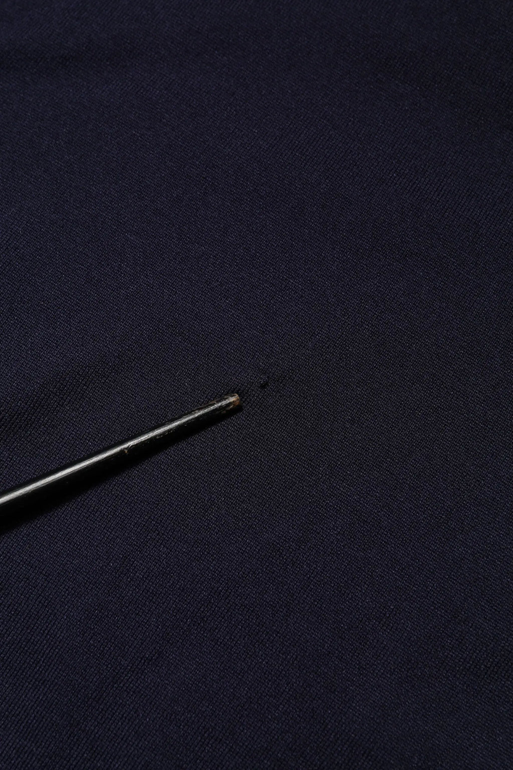 Une aiguille noire élégante avec une pointe métallique repose sur un t-shirt dolce & gabbana bleu marine en soie à manches courtes col rond