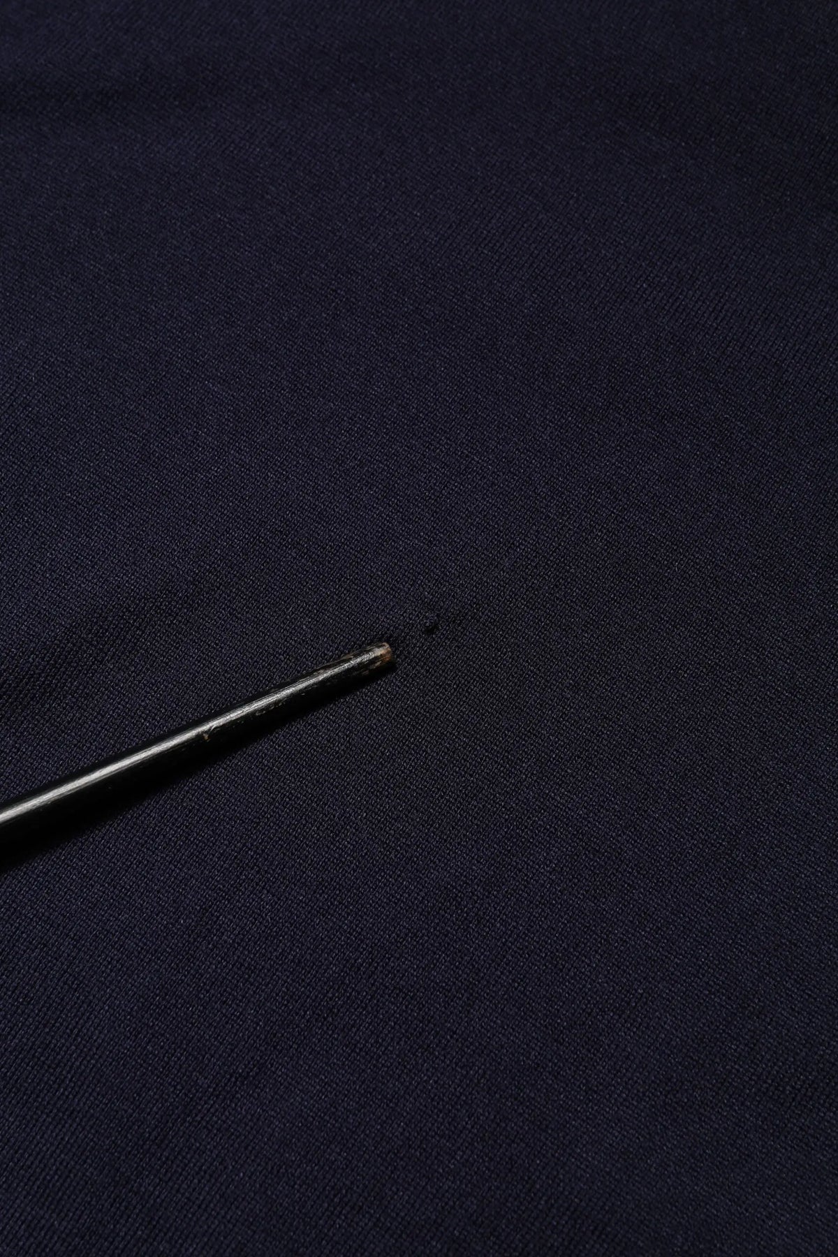Une aiguille noire élégante avec une pointe métallique repose sur un t-shirt dolce & gabbana bleu marine en soie à manches courtes col rond