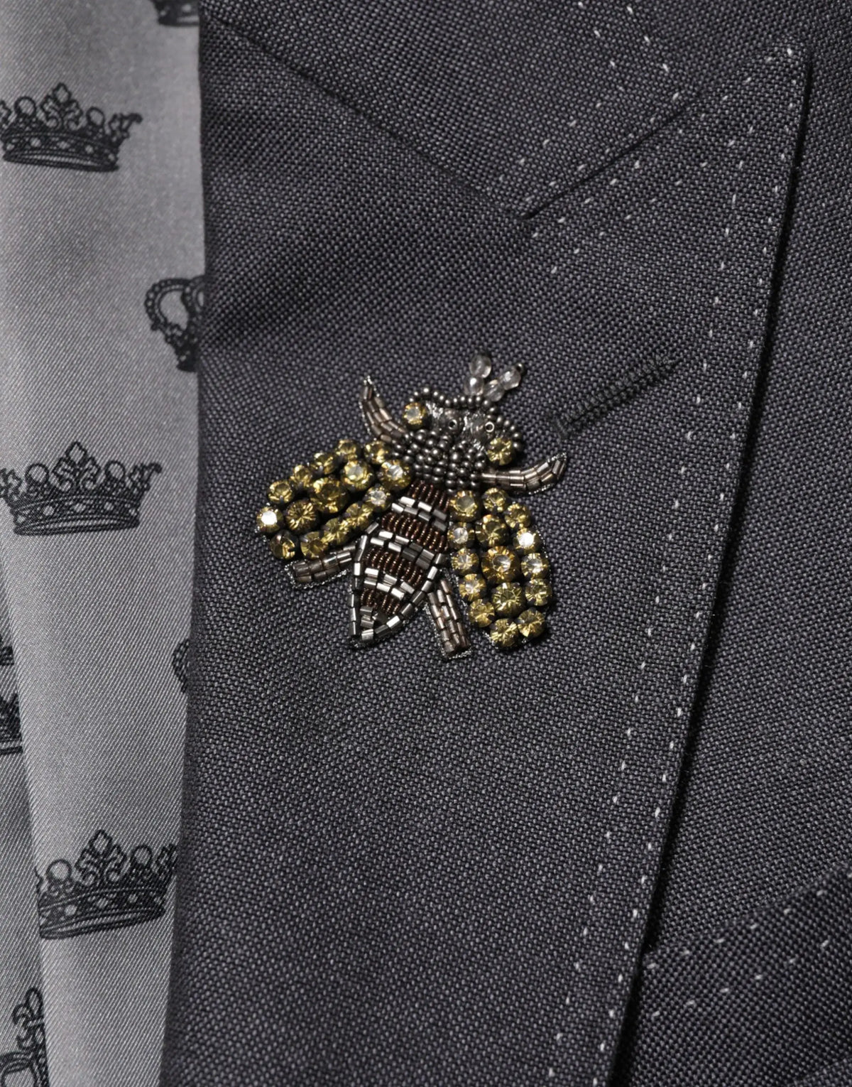 Une broche abeille détaillée perles avec accents or et noir orne un blazer en laine gris foncé dolce & gabbana