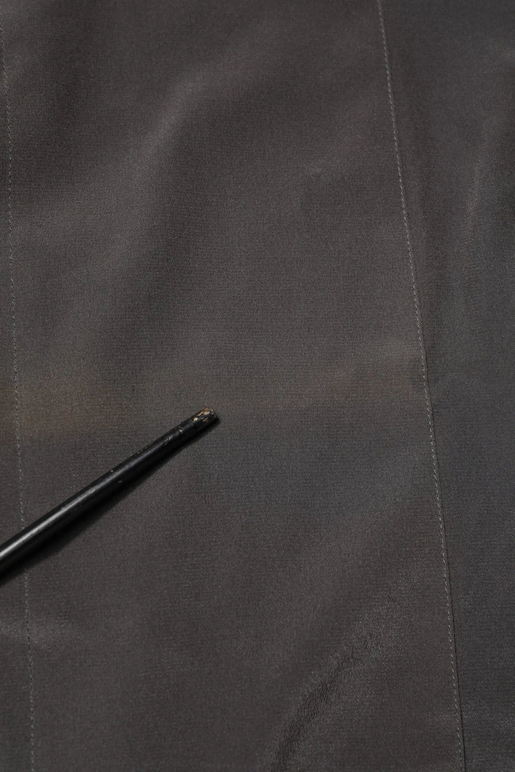 Bâton noir légèrement usé avec pointe texturée posé sur tissu gris foncé dans chemise formelle soie dolce gabbana