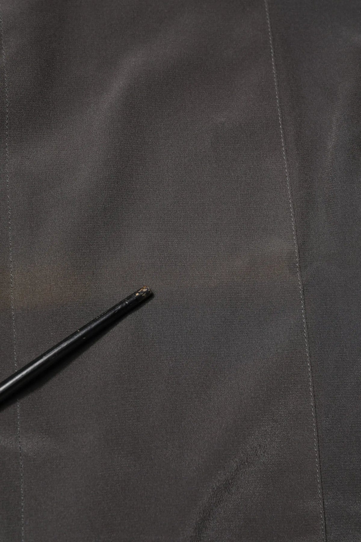Bâton noir légèrement usé avec pointe texturée posé sur tissu gris foncé dans chemise formelle soie dolce gabbana