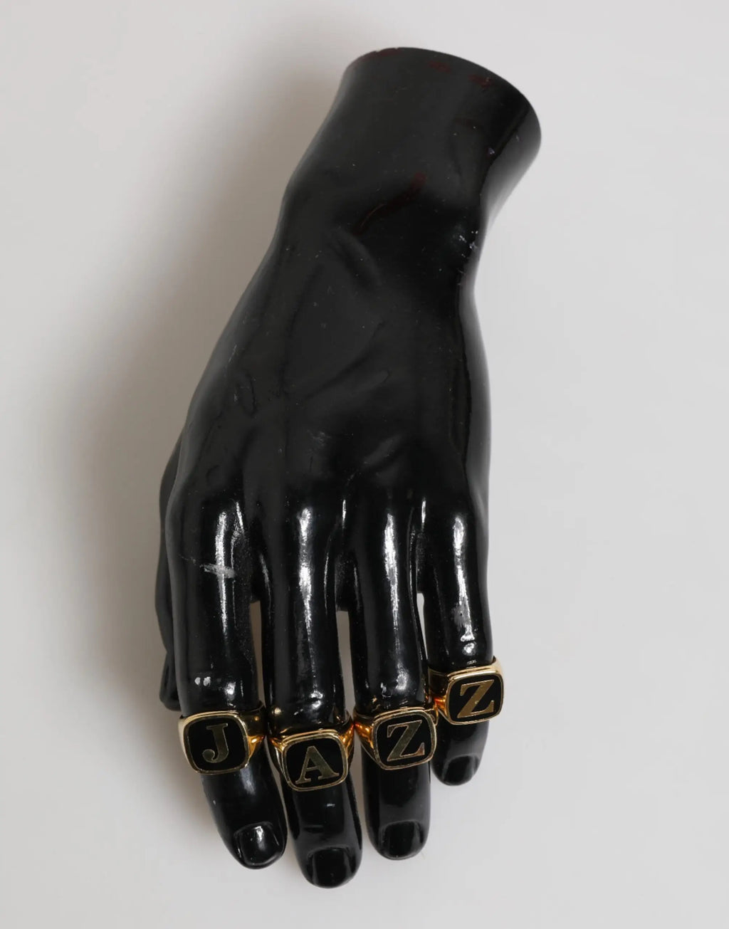 Mannequin main en résine noire brillante portant quatre bagues ajustables en laiton doré dolce gabbana avec lettres jazz