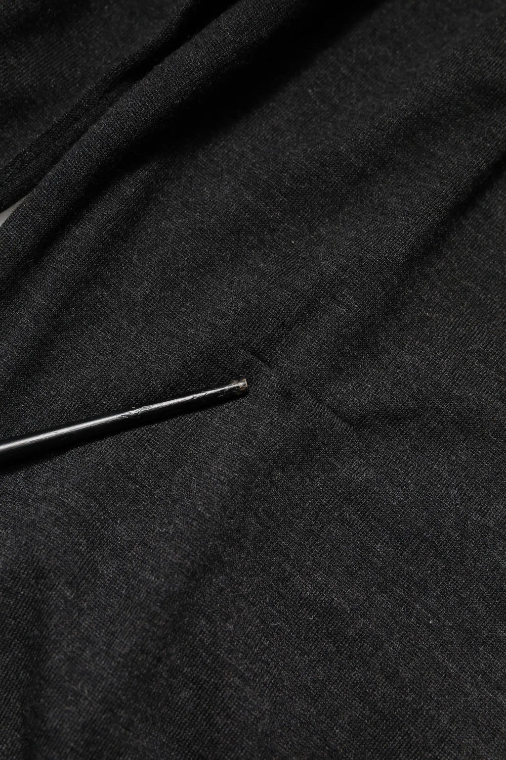 Une aiguille noire élégante posée sur un tissu gris foncé texturé du sweatshirt gris en cachemire Dolce & Gabbana