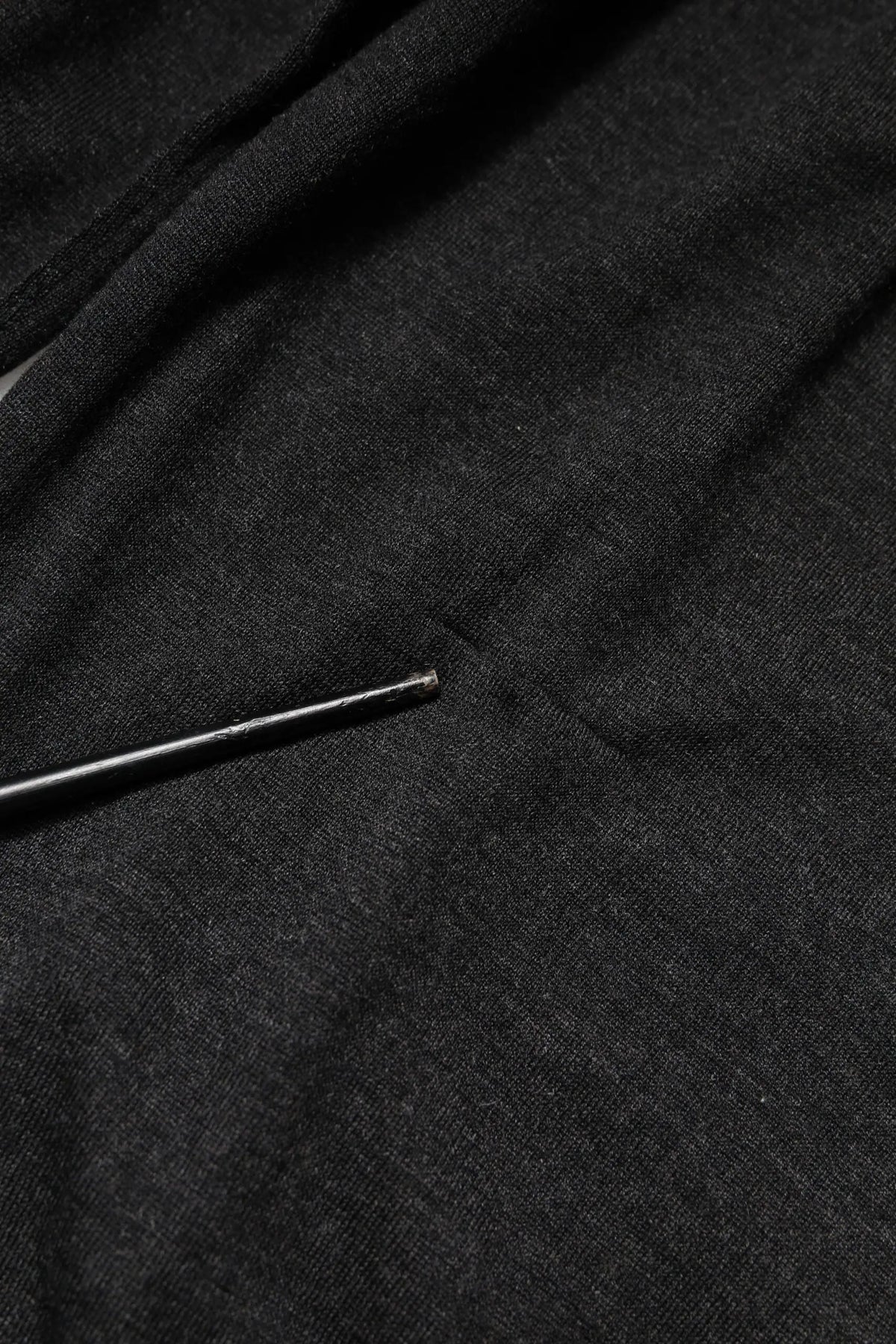 Une aiguille noire élégante posée sur un tissu gris foncé texturé du sweatshirt gris en cachemire Dolce & Gabbana