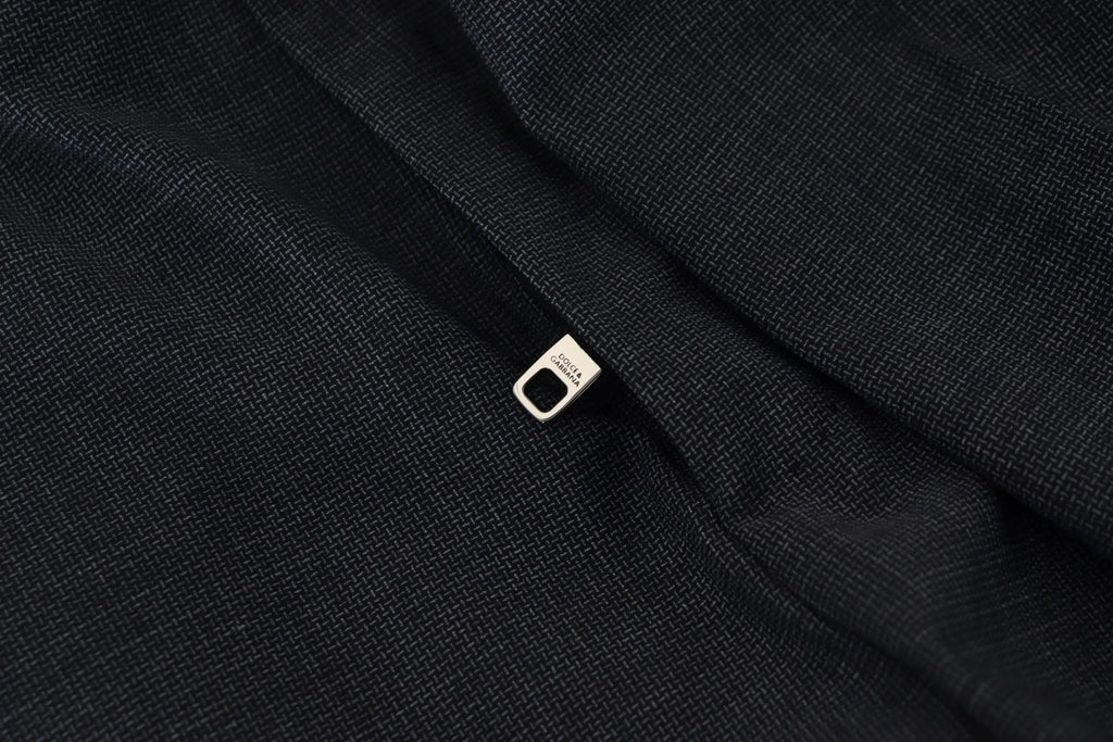 Une tirette de fermeture éclair en métal argenté minimaliste sur un tissu texturé foncé d’une veste de costume dolce gabbana