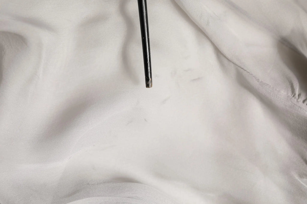 Bâtonnets noirs métalliques reposant sur tissu blanc près d’un chemisier gris en mousseline de soie dolce gabbana