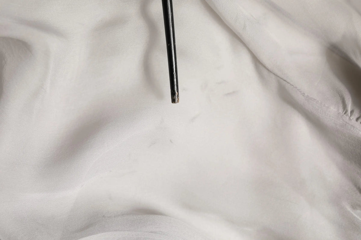 Bâtonnets noirs métalliques reposant sur tissu blanc près d’un chemisier gris en mousseline de soie dolce gabbana