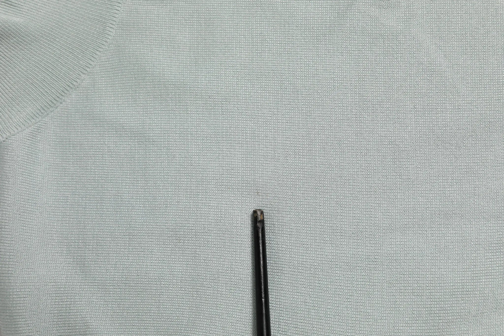 Aiguille à coudre noire fine posée sur tissu gris clair à texture sous un pull dolce & gabbana gris col roulé manches 3 4